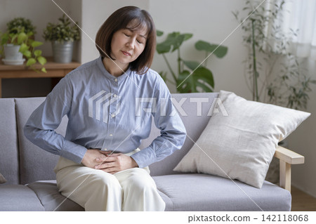 A woman in her early 50s holding her lower abdomen A woman in her early 50s holding her lower abdomen 142118068