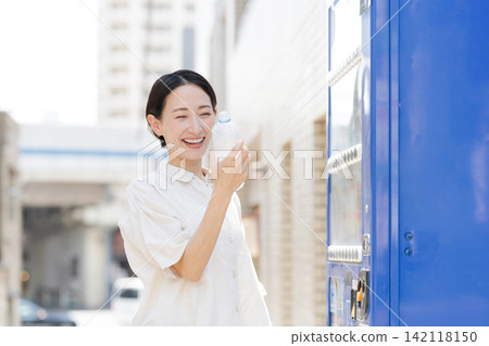 一位女士正在喝她從自動販賣機買的水。 一位女士正在喝她從自動販賣機買的水。 142118150
