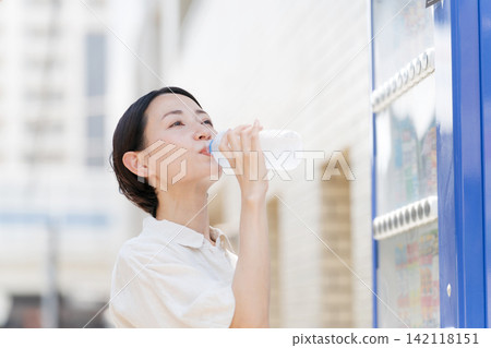 A woman drinking water she bought from a vending machine. A woman drinking water she bought from a vending machine. 142118151