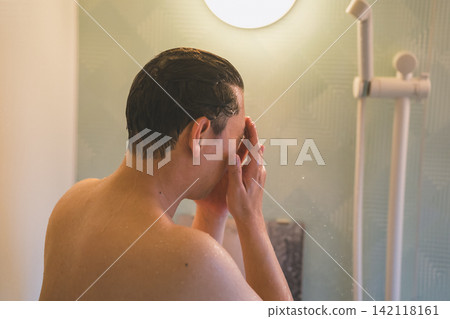 A man in his 40s washing his face in the shower, seen from behind. A man in his 40s washing his face in the shower, seen from behind. 142118161