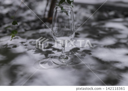 一隻空酒杯放在桌上,投下植物的影子。 一隻空酒杯放在桌上,投下植物的影子。 142118361