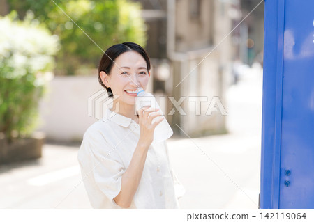 一位女士正在喝她從自動販賣機買的水。 142119064