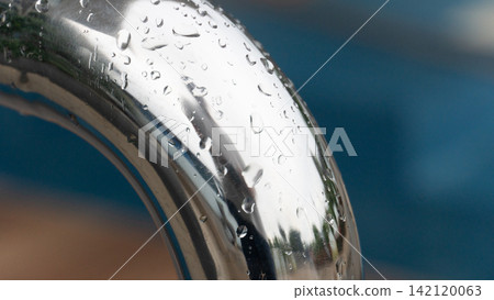 Curved stainless steel pipe featuring a smooth. Polished surface speckled with scattered raindrops. Curved stainless steel pipe featuring a smooth. Polished surface speckled with scattered raindrops. 142120063