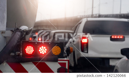 Close up rear view of a utility truck with glowing warning lights stopped in urban traffic. Many cars were parked in a queue. A concrete overpass stood beside them all under a bright blue sky. Close up rear view of a utility truck with glowing warning lights stopped in urban traffic. Many cars were parked in a queue. A concrete overpass stood beside them all under a bright blue sky. 142120066