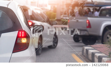 Rear side of white car with turn on right signal waiting to make a U-turn. Cars are stopped in a heavy traffic queue on a city street during a busy daytime commute with bright sunlight. Rear side of white car with turn on right signal waiting to make a U-turn. Cars are stopped in a heavy traffic queue on a city street during a busy daytime commute with bright sunlight. 142120068
