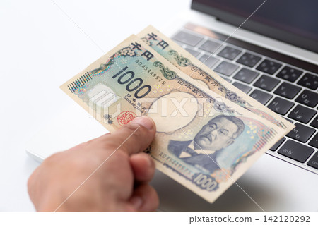 A hand holding 2,000 yen in front of a computer. A hand holding 2,000 yen in front of a computer. 142120292
