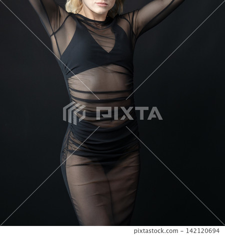 Dancer wearing transparent black dress posing on black background Dancer wearing transparent black dress posing on black background 142120694