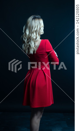 Elegant blonde woman posing in red dress on black background 142120805