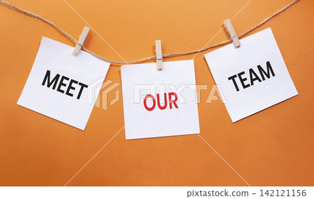 Meet Our Team text on white paper notes hanging on rope with clothespins over orange background. Team introduction and corporate culture concept with copy space. Meet Our Team text on white paper notes hanging on rope with clothespins over orange background. Team introduction and corporate culture concept with copy space. 142121156