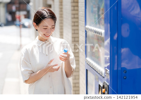 一位女士正在喝她從自動販賣機買的水。 一位女士正在喝她從自動販賣機買的水。 142121954