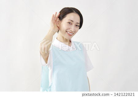 A female caregiver with her hand to her ear against a white background. A female caregiver with her hand to her ear against a white background. 142122021