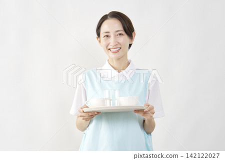 一位女護理員在白色背景下為客人準備餐點。 142122027