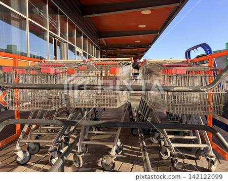 Row of empty metal shopping carts with red handles parked outside a modern supermarket Row of empty metal shopping carts with red handles parked outside a modern supermarket 142122099