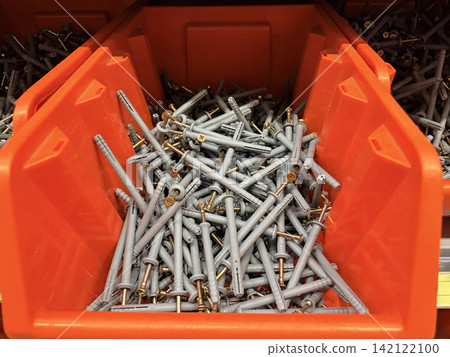 plastic wall plugs and gold screws piled in an orange bin at a hardware store 142122100