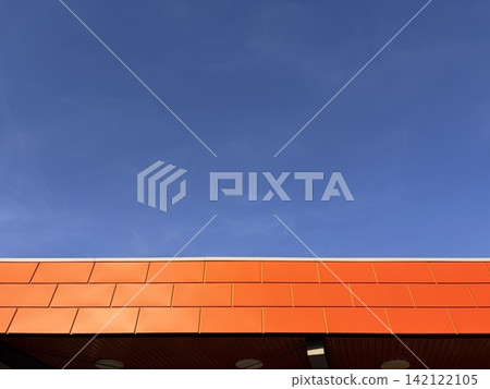 Low angle view of modern building roofline with bright orange panels against a clear blue sky Low angle view of modern building roofline with bright orange panels against a clear blue sky 142122105