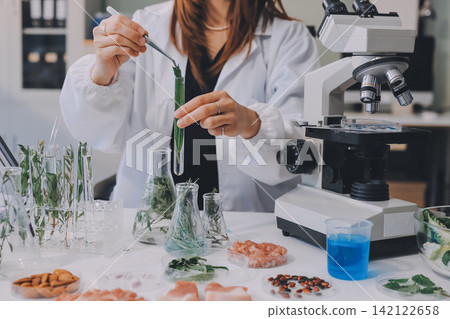 Scientists in lab coats work with plants in a modern lab, focusing on research and experimentation under bright, sterile conditions. Scientists in lab coats work with plants in a modern lab, focusing on research and experimentation under bright, sterile conditions. 142122658