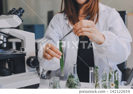 Scientists in lab coats work with plants in a modern lab, focusing on research and experimentation under bright, sterile conditions. Scientists in lab coats work with plants in a modern lab, focusing on research and experimentation under bright, sterile conditions. 142122659
