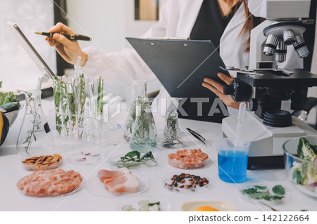 Scientists in lab coats work with plants in a modern lab, focusing on research and experimentation under bright, sterile conditions. Scientists in lab coats work with plants in a modern lab, focusing on research and experimentation under bright, sterile conditions. 142122664