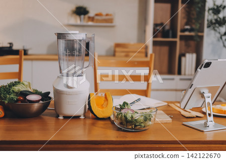 Woman preparing green smoothie in bright kitchen with fresh fruits and vegetables, healthy eating lifestyle moment in natural daylight Woman preparing green smoothie in bright kitchen with fresh fruits and vegetables, healthy eating lifestyle moment in natural daylight 142122670