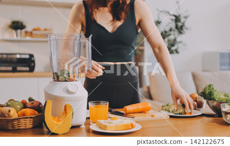 Woman preparing green smoothie in bright kitchen with fresh fruits and vegetables, healthy eating lifestyle moment in natural daylight Woman preparing green smoothie in bright kitchen with fresh fruits and vegetables, healthy eating lifestyle moment in natural daylight 142122675