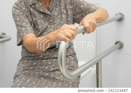 Asian elderly woman use toilet security support rail in bathroom. Asian elderly woman use toilet security support rail in bathroom. 142123487