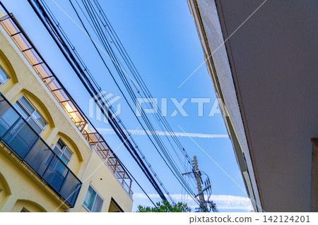 Blue sky and contrails stretching between buildings and power lines Blue sky and contrails stretching between buildings and power lines 142124201