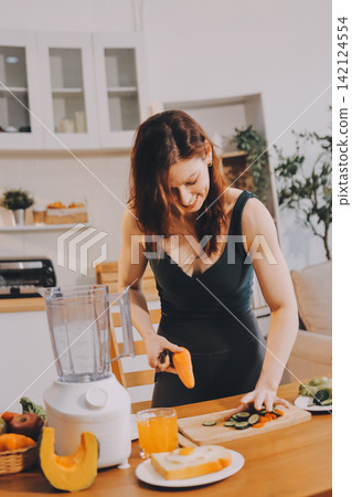 Woman preparing green smoothie in bright kitchen with fresh fruits and vegetables, healthy eating lifestyle moment in natural daylight Woman preparing green smoothie in bright kitchen with fresh fruits and vegetables, healthy eating lifestyle moment in natural daylight 142124554