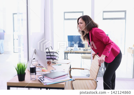 Businesswoman leaning over office desk and studying computer monitor in bright modern workspace with papers, keyboard, chair, and sunlight streaming through glass walls during busy workday Businesswoman leaning over office desk and studying computer monitor in bright modern workspace with papers, keyboard, chair, and sunlight streaming through glass walls during busy workday 142124860