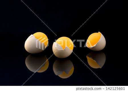 Still life with eggshell and orange balls on a black background 142125601