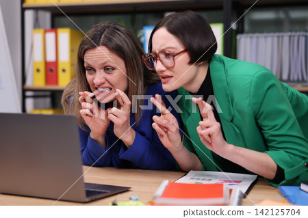 Two frustrated coworkers lean over laptop in modern office, studying charts, documents, and business materials with tense focused expressions during serious workplace discussion Two frustrated coworkers lean over laptop in modern office, studying charts, documents, and business materials with tense focused expressions during serious workplace discussion 142125704