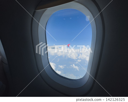 Airplane window. View of sky from inside of airplane. Airplane wing and sky clouds earth view. Blue clear sky and wings of plane window view. Tourism travel journey trip 142126325