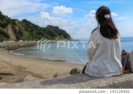 一位女子站在海堤上,凝望著蔚藍的大海和沙灘。 一位女子站在海堤上,凝望著蔚藍的大海和沙灘。 142126462
