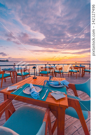 Elegant beach restaurant table setting glowing pastel dusk overwater terrace calm azure Maldives sea. Luxury honeymoon travel paradise scenic. Exotic couples getaway decor wallpaper Elegant beach restaurant table setting glowing pastel dusk overwater terrace calm azure Maldives sea. Luxury honeymoon travel paradise scenic. Exotic couples getaway decor wallpaper 142127496