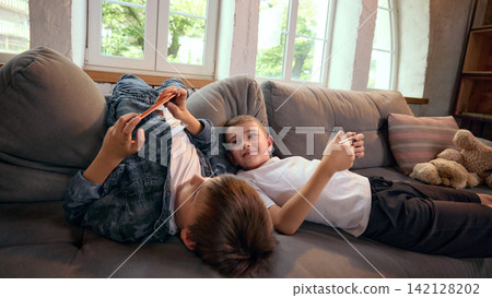 Two boys reclining on sofa while using smartphones during free time Two boys reclining on sofa while using smartphones during free time 142128202