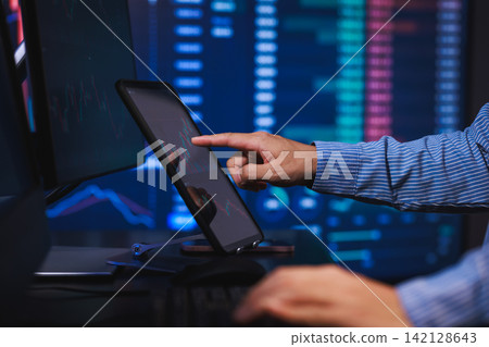 Hand pointing at a tablet on a desk with blurred stock market charts on monitors in the background, trading and financial analysis Hand pointing at a tablet on a desk with blurred stock market charts on monitors in the background, trading and financial analysis 142128643