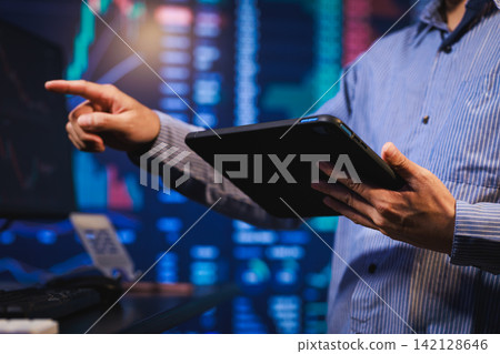 Businessman holding a tablet and pointing at a screen in a server room with blurred data center lights Businessman holding a tablet and pointing at a screen in a server room with blurred data center lights 142128646