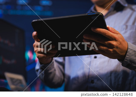 Close-up of a person holding a tablet in a dark office with blue screen light, a modern business or tech workspace and hands using a digital device Close-up of a person holding a tablet in a dark office with blue screen light, a modern business or tech workspace and hands using a digital device 142128648