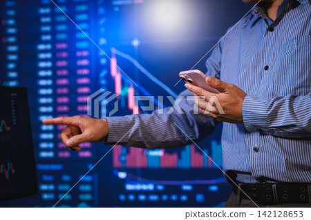 Man holding a smartphone and pointing at stock market charts on a screen, finance analysis and trading data. Man holding a smartphone and pointing at stock market charts on a screen, finance analysis and trading data. 142128653