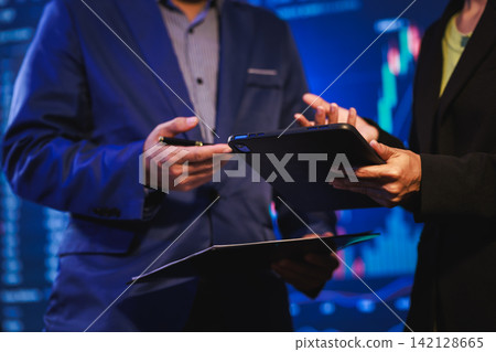 Close-up of business people in suits discussing a tablet and documents in a modern office with blue digital background Close-up of business people in suits discussing a tablet and documents in a modern office with blue digital background 142128665