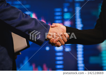 Closeup of a business handshake in front of a stock market chart display, symbolizing agreement, finance, investment and partnership. 142128669