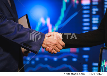 Business handshake in front of stock market charts on screens Business handshake in front of stock market charts on screens 142128670
