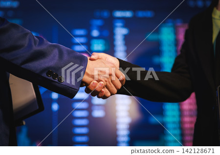 Business handshake between two people with blurred stock market screens in the background, symbolizing agreement, finance, trading, and partnership Business handshake between two people with blurred stock market screens in the background, symbolizing agreement, finance, trading, and partnership 142128671