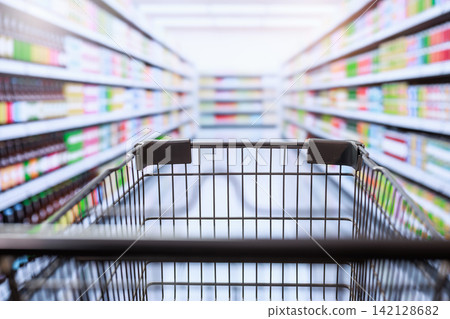 Shopping cart in a grocery store aisle with blurred shelves and bright supermarket lights, a wide selection of products in a clean retail setting Shopping cart in a grocery store aisle with blurred shelves and bright supermarket lights, a wide selection of products in a clean retail setting 142128682