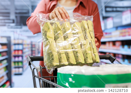 Person placing a large bag of packaged snacks into a shopping cart in a supermarket aisle Person placing a large bag of packaged snacks into a shopping cart in a supermarket aisle 142128710