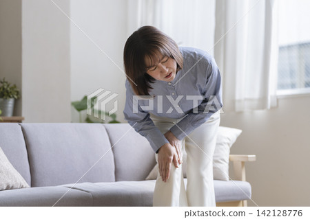 A woman in her late 40s with her hands on her knees and thighs, grimacing. A woman in her late 40s with her hands on her knees and thighs, grimacing. 142128776