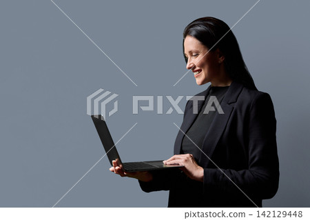 Smiling businesswoman using laptop computer side profile view in studio Smiling businesswoman using laptop computer side profile view in studio 142129448