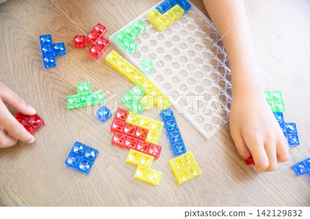 A child's hands playing with a colorful block puzzle. A child's hands playing with a colorful block puzzle. 142129832