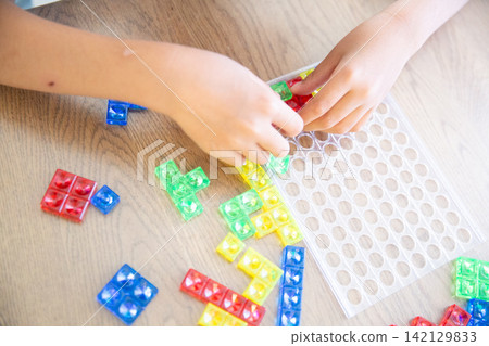 A child's hands playing with a colorful block puzzle. A child's hands playing with a colorful block puzzle. 142129833