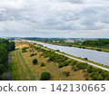 Aerial view of Mittellandkanal fork in Magdeburg with calm waterway, embankments, paths and dry summer grass. Broad canal landscape stretches beneath layered clouds, greenery and distant ships 142130665