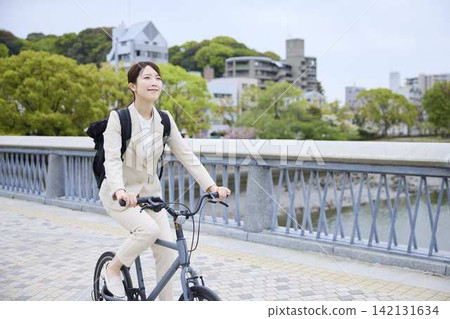 一位女商人推著自行車,沿著河邊的橋行走。 一位女商人推著自行車,沿著河邊的橋行走。 142131634